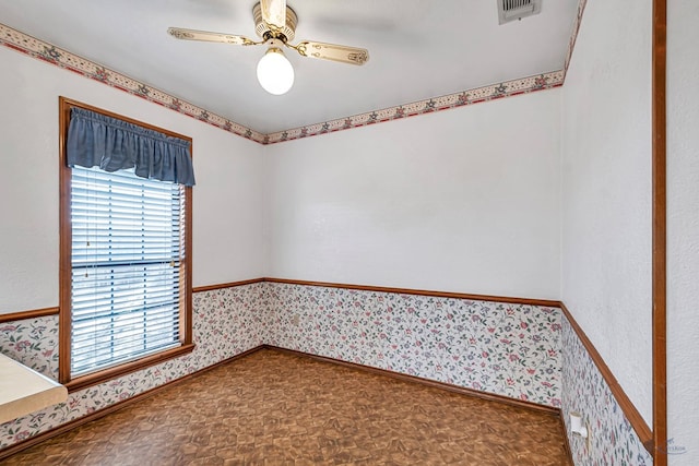 empty room featuring wallpapered walls, a wainscoted wall, a ceiling fan, and visible vents