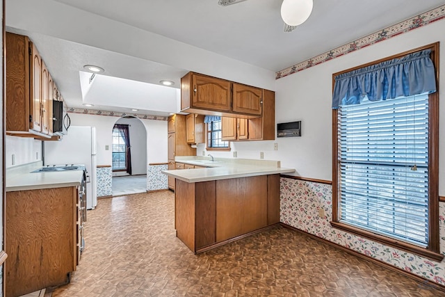 kitchen with gas stove, a peninsula, arched walkways, a sink, and light countertops