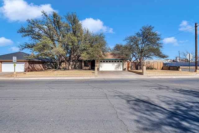 view of front facade featuring an attached garage, concrete driveway, and fence