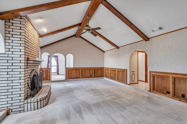 unfurnished living room with a wainscoted wall, vaulted ceiling with beams, arched walkways, light carpet, and a brick fireplace