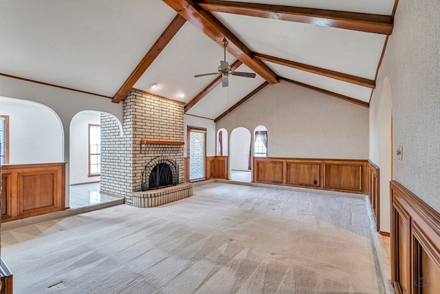 unfurnished living room with high vaulted ceiling, beam ceiling, a fireplace, ceiling fan, and light colored carpet