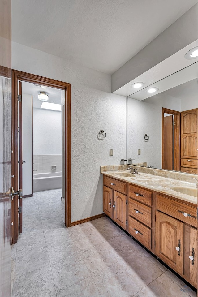 full bathroom featuring baseboards, a textured wall, and double vanity