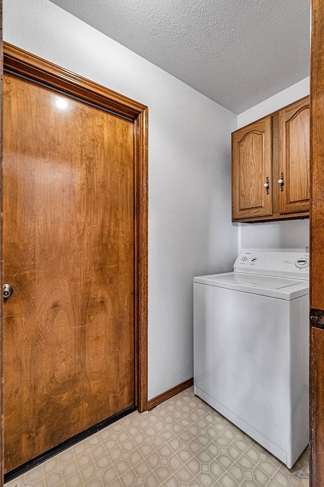 washroom with light floors, baseboards, washer / dryer, cabinet space, and a textured ceiling