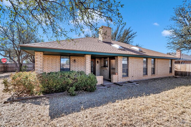 back of property featuring a shingled roof, fence, brick siding, and a chimney