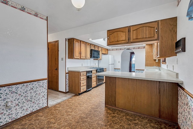 kitchen with black microwave, light countertops, brown cabinets, arched walkways, and stove