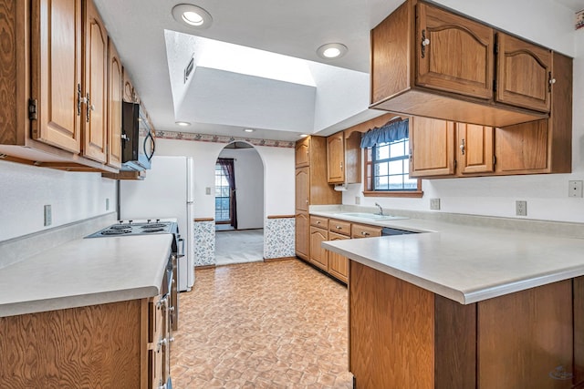 kitchen featuring black microwave, light countertops, a peninsula, arched walkways, and a sink