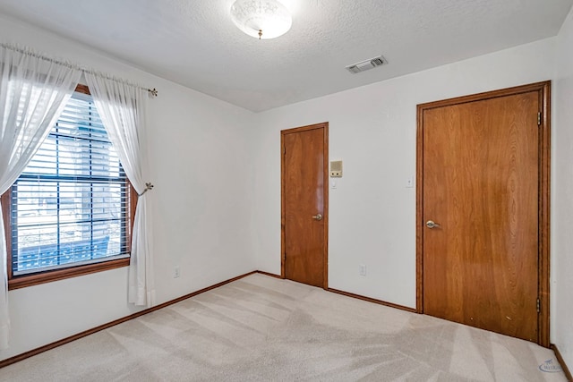 spare room with a textured ceiling, baseboards, visible vents, and light carpet