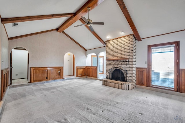 unfurnished living room featuring beamed ceiling, visible vents, wainscoting, light colored carpet, and a brick fireplace