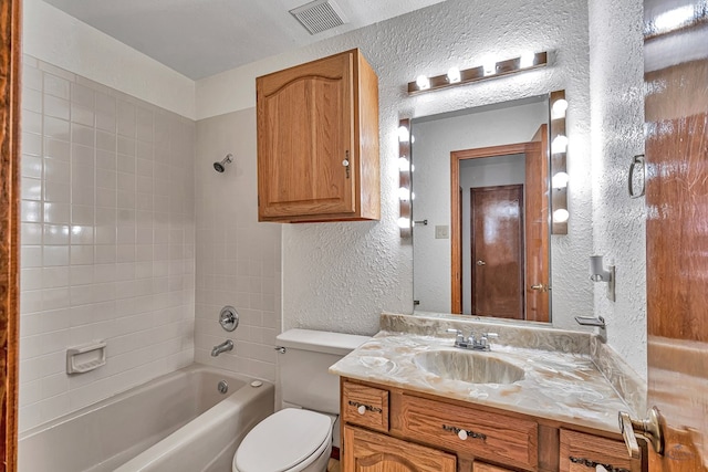 bathroom featuring vanity, visible vents,  shower combination, toilet, and a textured wall