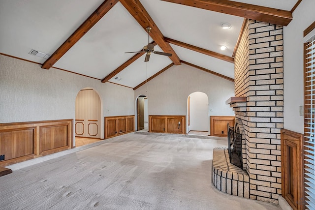 unfurnished living room featuring a wainscoted wall, visible vents, lofted ceiling with beams, arched walkways, and light colored carpet