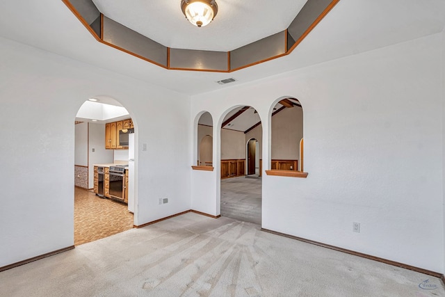 unfurnished room with baseboards, visible vents, arched walkways, a raised ceiling, and light colored carpet