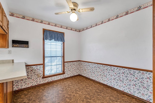 unfurnished room with a wainscoted wall, baseboards, a ceiling fan, and wallpapered walls