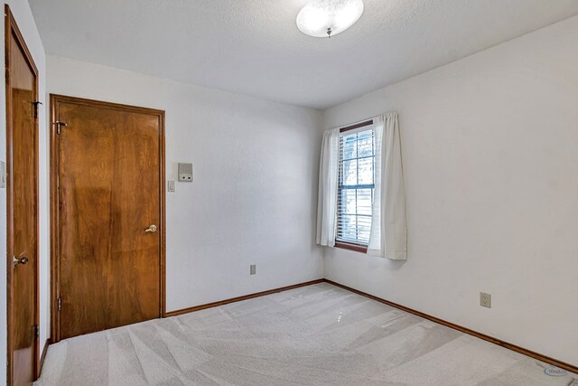 spare room with baseboards, light colored carpet, and a textured ceiling