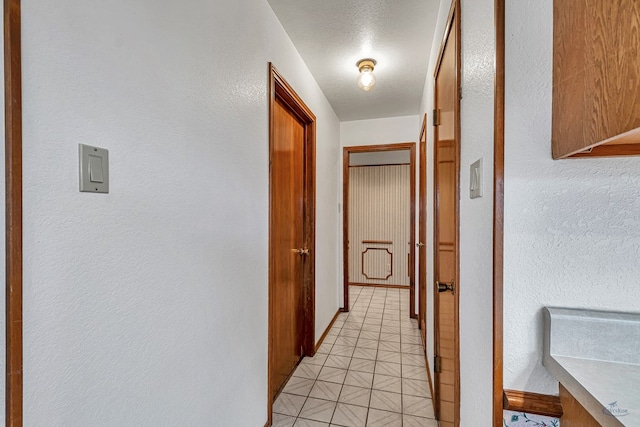 hallway featuring light floors, a textured ceiling, and a textured wall