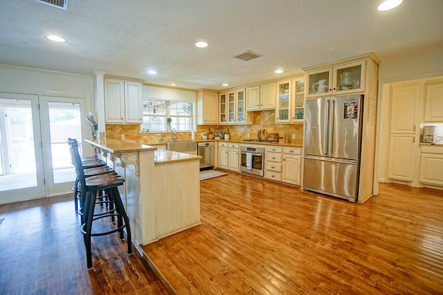 kitchen with stainless steel appliances, wood finished floors, a breakfast bar, a peninsula, and tasteful backsplash