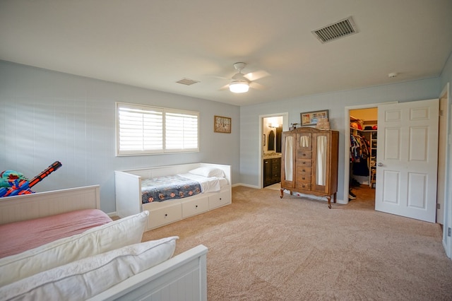 bedroom featuring a walk in closet, light carpet, a closet, ceiling fan, and ensuite bathroom