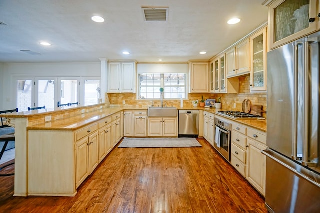 kitchen featuring appliances with stainless steel finishes, a sink, a kitchen breakfast bar, a peninsula, and wood finished floors