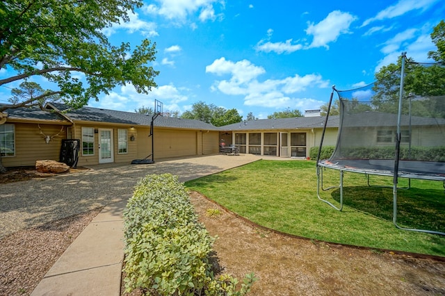 rear view of property featuring a trampoline, a garage, concrete driveway, a sunroom, and a lawn