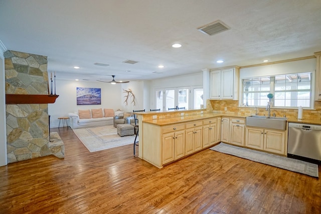 kitchen featuring dishwasher, a sink, light wood-style floors, open floor plan, and decorative backsplash