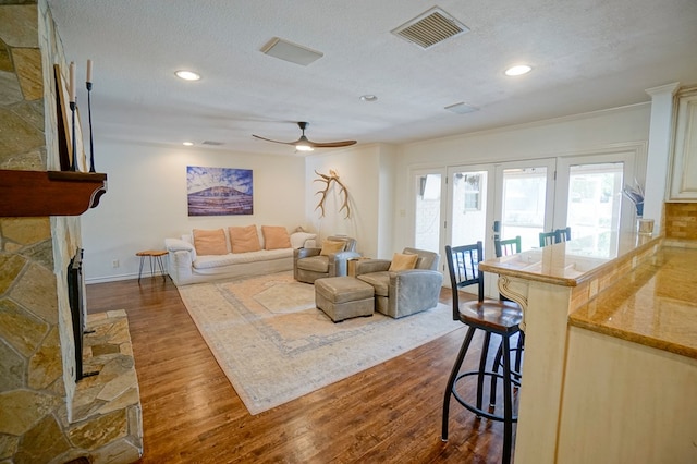 living area featuring dark wood-style floors, ceiling fan, a textured ceiling, a stone fireplace, and recessed lighting