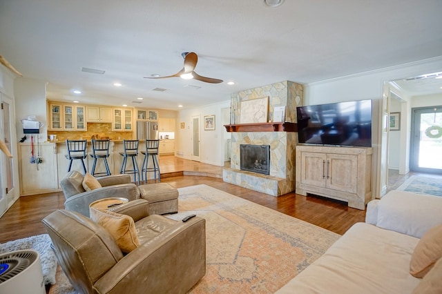living area featuring wood finished floors, a ceiling fan, crown molding, a fireplace, and recessed lighting