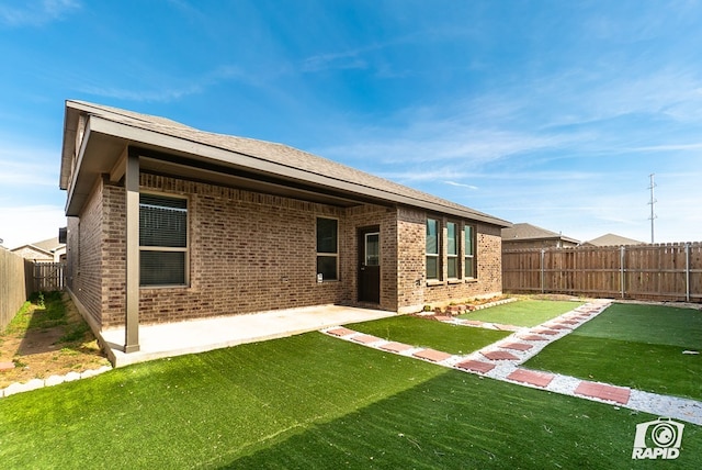rear view of house featuring a patio, brick siding, a fenced backyard, and a lawn