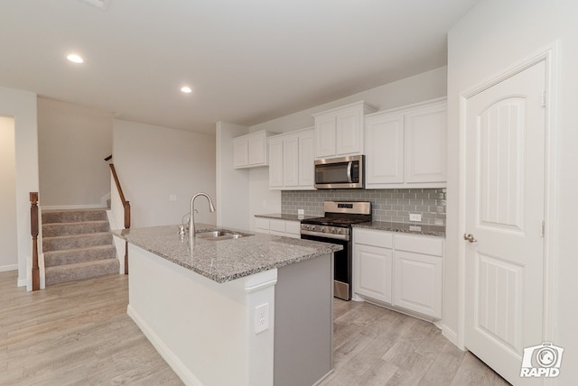 kitchen featuring a kitchen island with sink, light wood-style floors, white cabinets, a sink, and stainless steel appliances