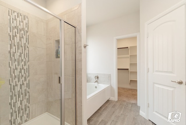 full bath featuring a garden tub, a stall shower, wood finished floors, and a walk in closet