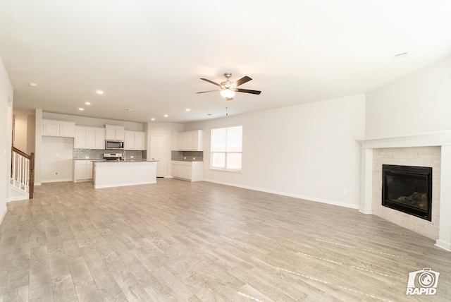 unfurnished living room featuring a brick fireplace, baseboards, ceiling fan, light wood-type flooring, and recessed lighting