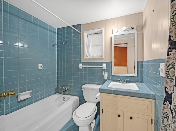 full bathroom with toilet, vanity, tiled shower / bath combo, and tile walls