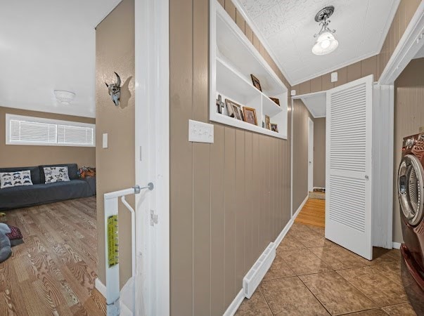 corridor with tile patterned flooring, wooden walls, washer / clothes dryer, and ornamental molding