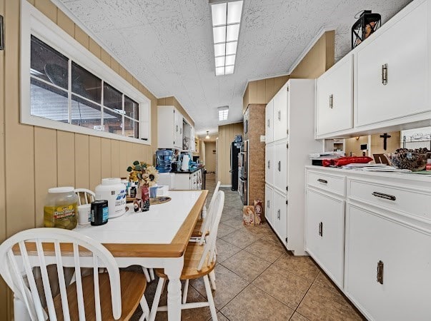 kitchen with white cabinetry, light tile patterned floors, and wood walls