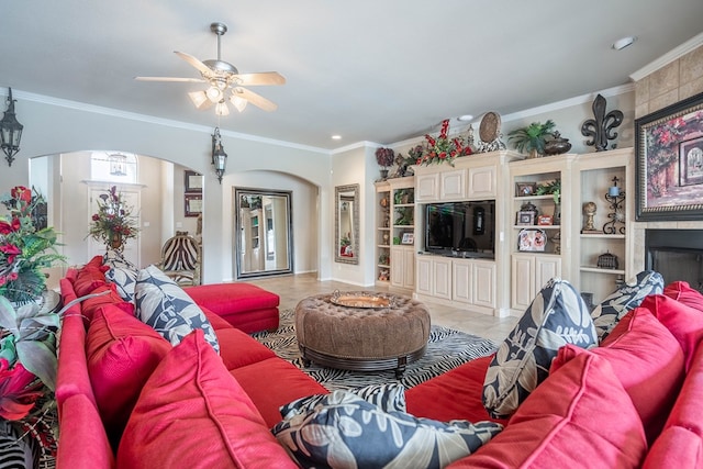 tiled living room with ceiling fan, a large fireplace, and ornamental molding