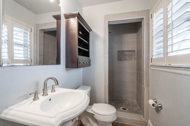 bathroom featuring tiled shower, sink, and toilet