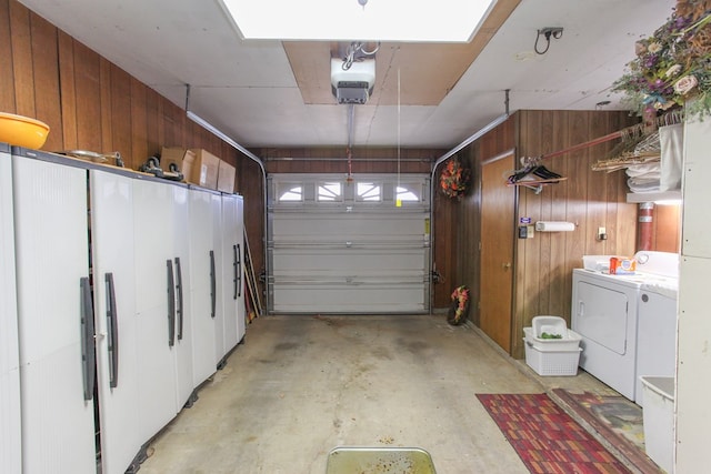 garage with a garage door opener, wood walls, and washer and clothes dryer