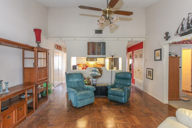 living area featuring baseboards, visible vents, a towering ceiling, and ceiling fan