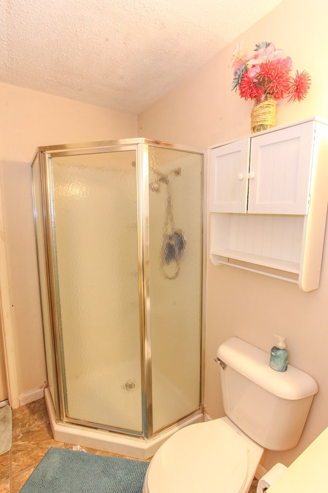 bathroom with a textured ceiling, a stall shower, and toilet