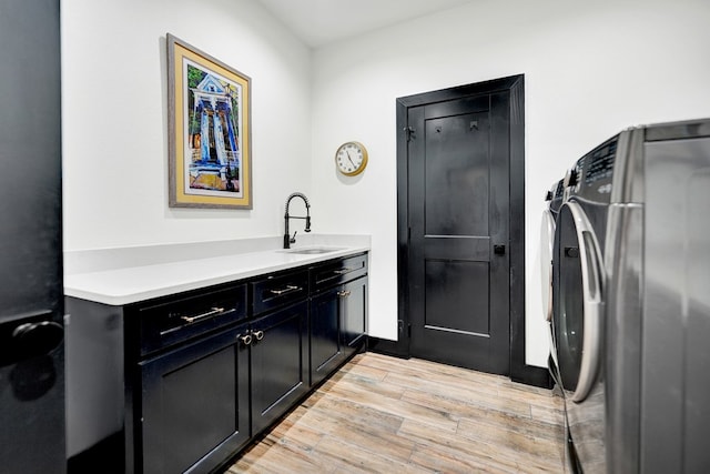 clothes washing area featuring light wood-type flooring, washing machine and clothes dryer, cabinet space, and a sink