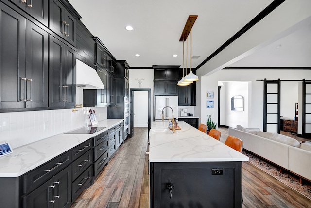 kitchen featuring a barn door, decorative backsplash, black electric cooktop, dark cabinets, and open floor plan
