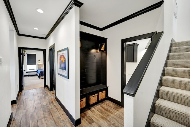 hallway featuring baseboards, light wood-type flooring, ornamental molding, and stairway