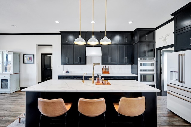 kitchen featuring light stone counters, high end white fridge, dark cabinetry, and ventilation hood