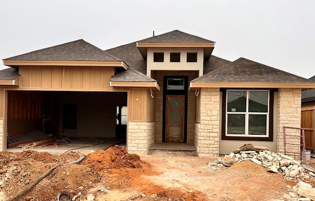 prairie-style home featuring board and batten siding, stone siding, roof with shingles, and an attached garage