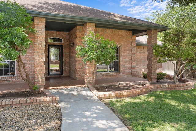 view of exterior entry featuring covered porch and a lawn