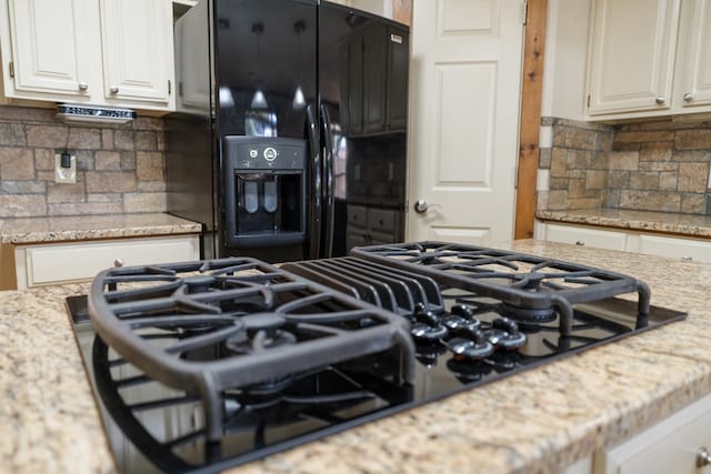 kitchen featuring decorative backsplash, white cabinets, light stone counters, and black appliances