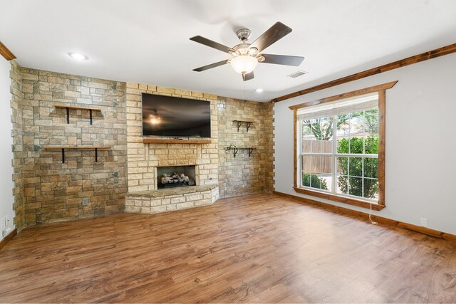 unfurnished living room with a stone fireplace, ceiling fan, wood-type flooring, and ornamental molding