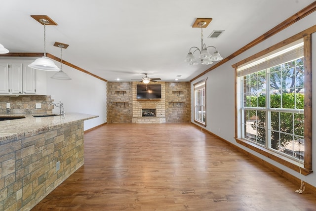 unfurnished living room with wood-type flooring, ceiling fan with notable chandelier, crown molding, and sink