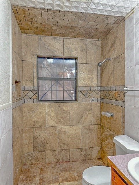 bathroom with vanity, toilet, tiled shower, and tile walls