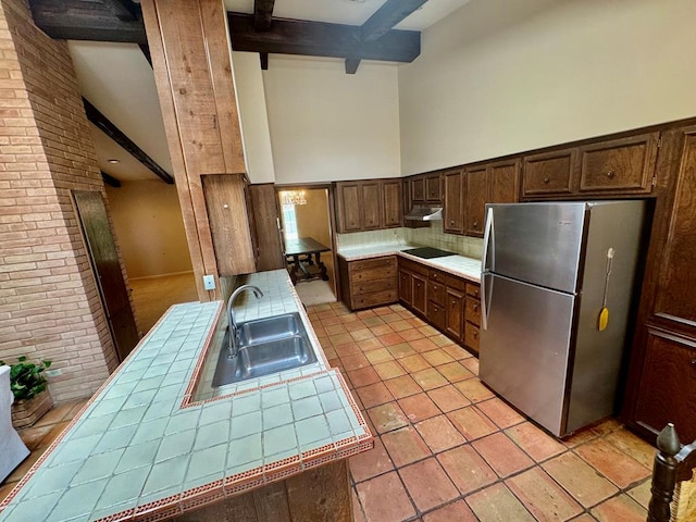 kitchen featuring tile counters, sink, beamed ceiling, high vaulted ceiling, and stainless steel fridge