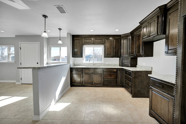 kitchen featuring decorative light fixtures, sink, light tile patterned floors, dark brown cabinets, and light stone counters