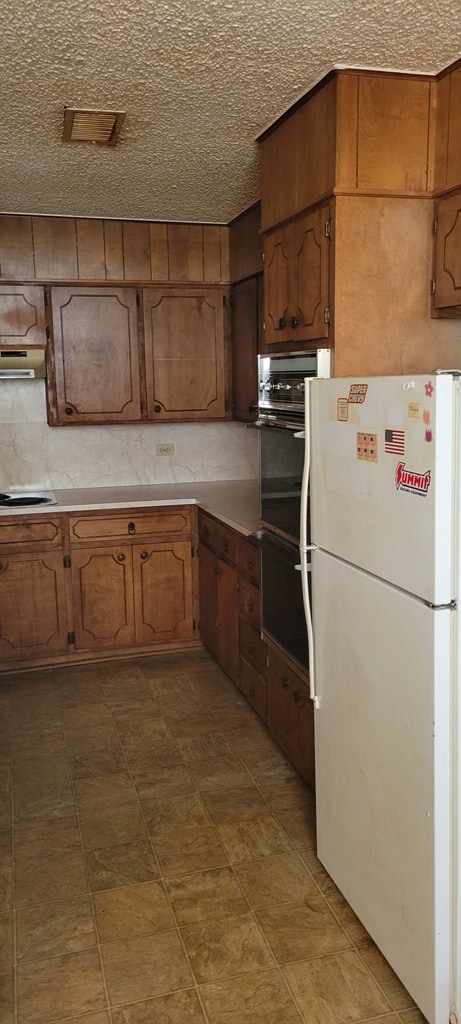 kitchen featuring a textured ceiling, white fridge, and black double oven